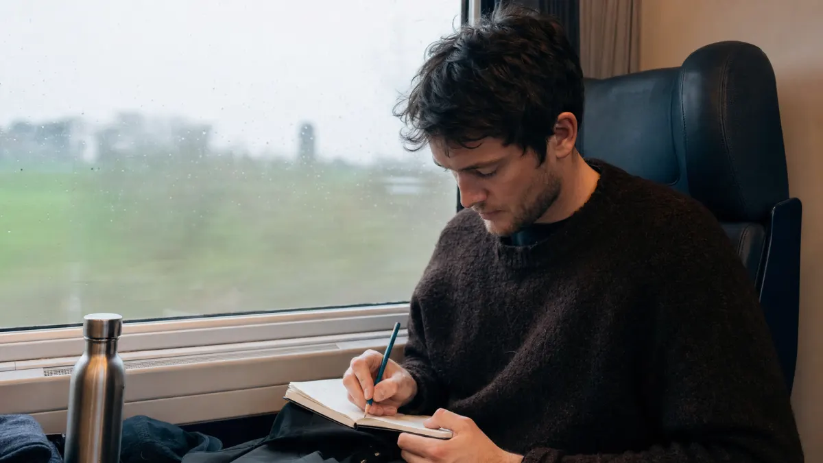 Student journals on a train while checking writing voice for a DecreaseAI review.