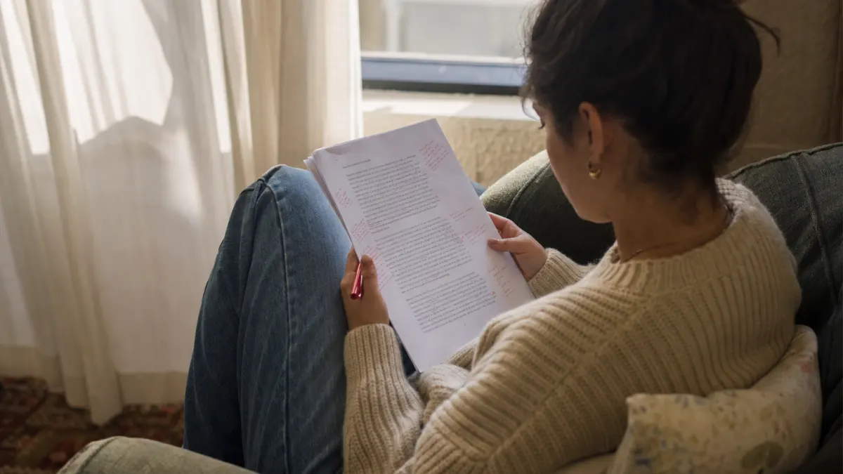 Student reviewing a printed article with handwritten notes in a sunlit armchair, evaluating whether to humanize AI text online before submission