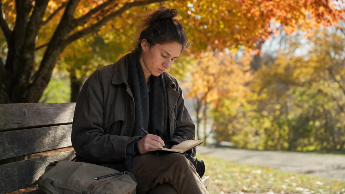 Young writer drafting on a park bench under autumn maples before deciding whether ChatGPT is detectable in their submission