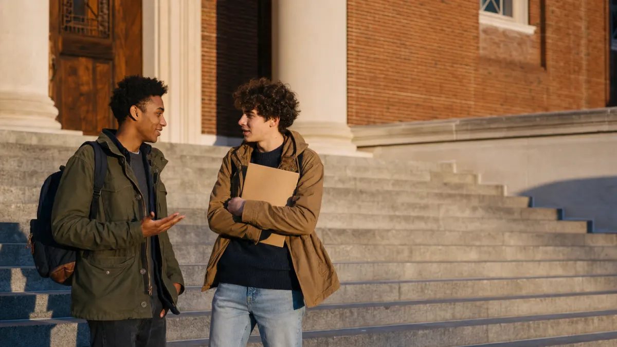 Two students talking on stone university steps about whether ChatGPT is detectable before they hand in their drafts